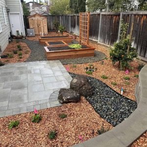 Beautiful backyard landscape with stone paving, raised garden beds, and decorative plants.
