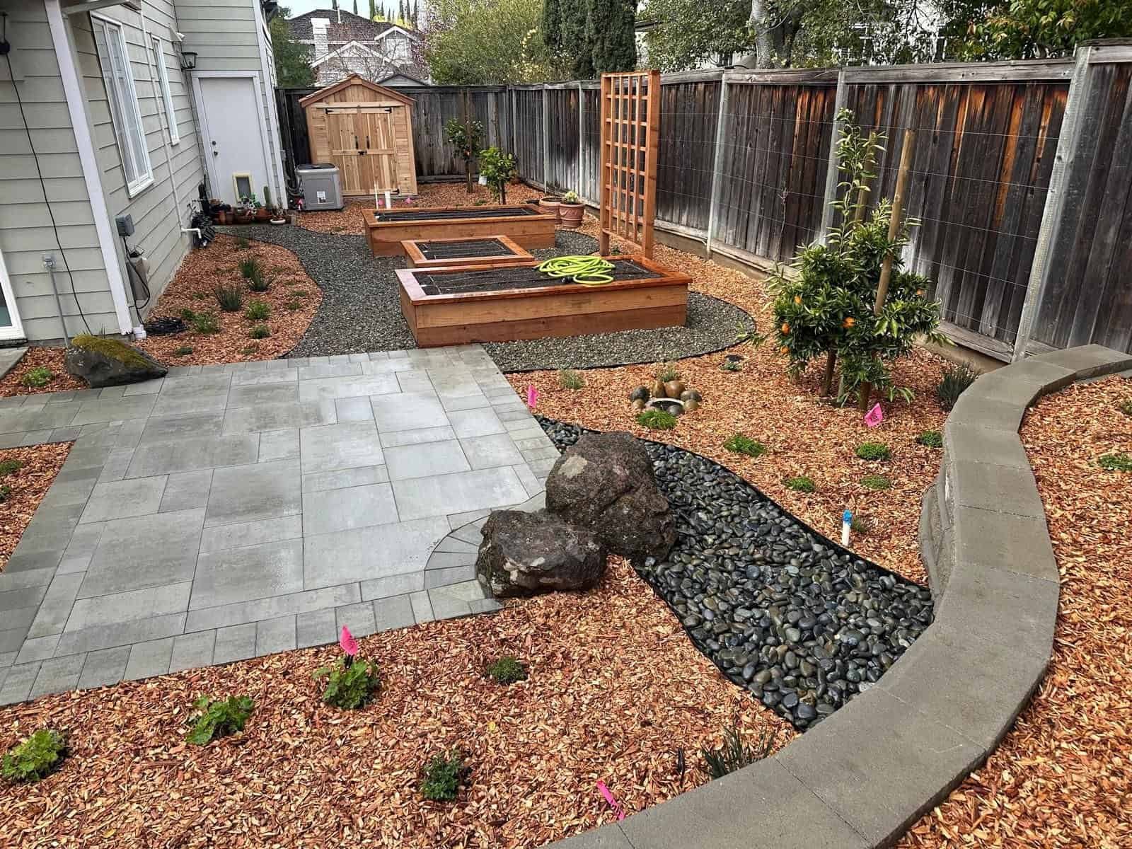 Beautiful backyard landscape with stone paving, raised garden beds, and decorative plants.